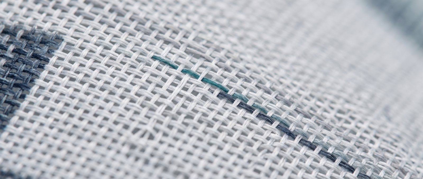 Macro photograph of pale woven cloth with a single teal thread running through it.